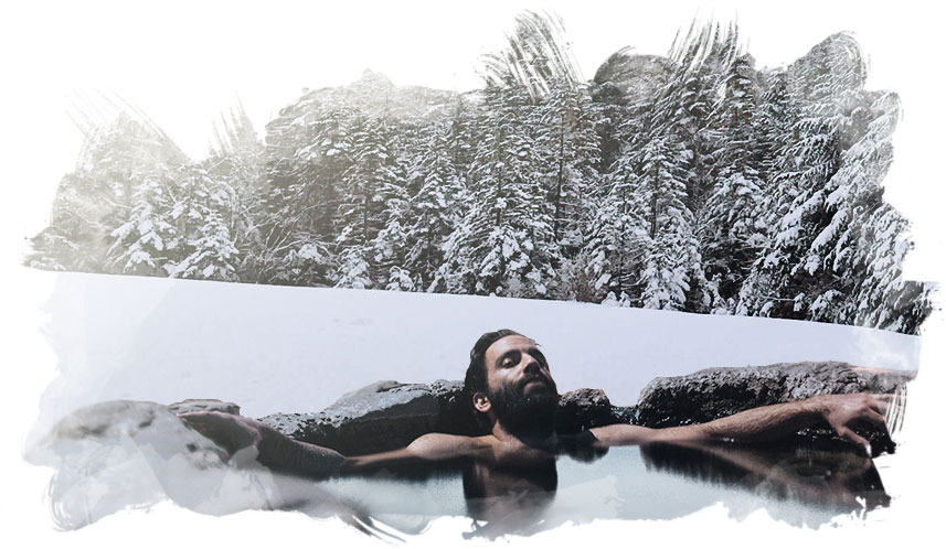 Man relaxing in a natural stone hottub, snowy wilderness in the background.
